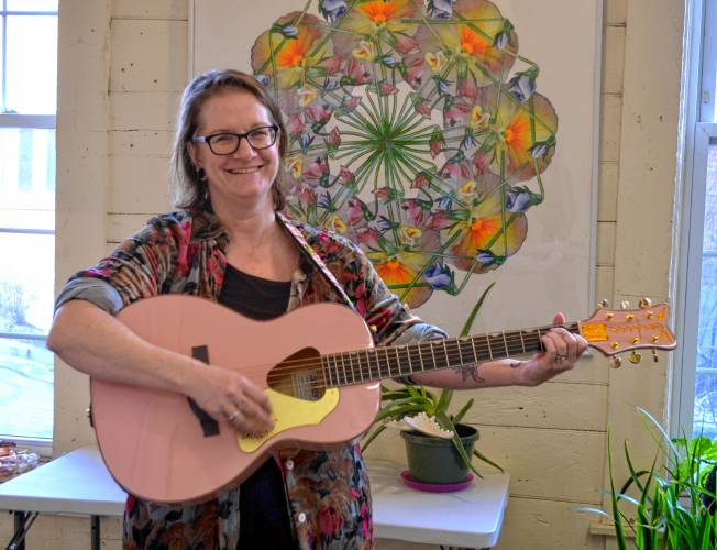 Kate Schimke with her guitar in front of a mandala.
