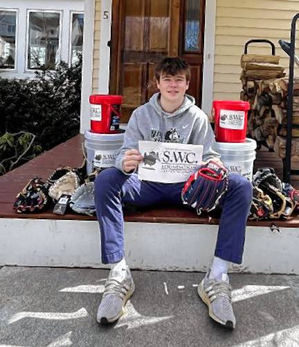 Jack Kidd holds a sign for the Steven W. Crowe Foundation while sitting with baseballs and gloves he and the foundation acquired for Mt. Monadnock Little League.