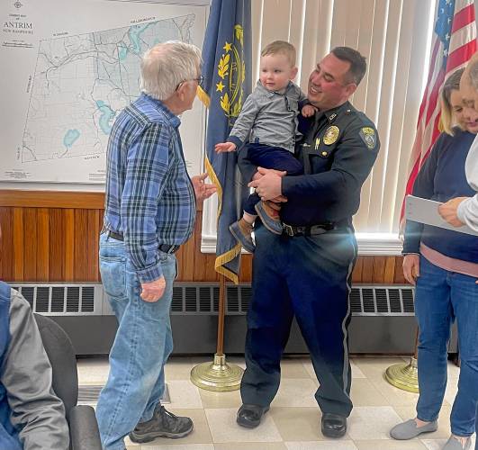 Antrim Select Board member John Robertson, left, says hello to Knox Blake, age 2, who is in the arms of his father, newly appointed Antrim Chief of Police John Blake. 