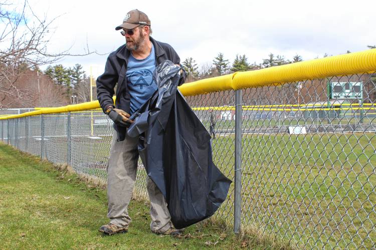 Matt Oliveira of New Ipswich picks up trash from the strip of green between the playground and ball field.