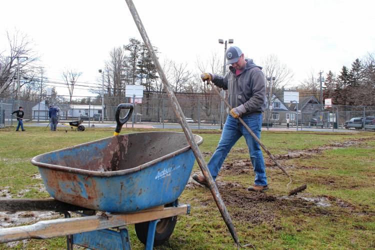John Pogorzelski of New Ipswich uses a wheelbarrow to remove rocks and debris from the ball field.