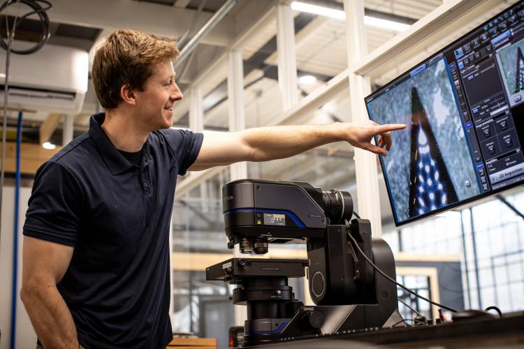 Evari team member Alex Reynolds points to images from a microscrope at the company’s manufacturing facility at Noone Falls. 