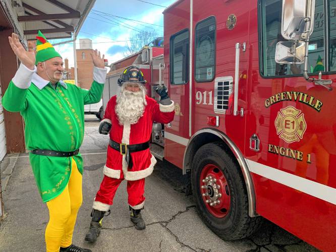 Charlie Jackman and Jim Feldhusen, as Buddy the Elf and Firefighter Santa, wave to passing cars before starting the tour atop the Greenville fire engine.